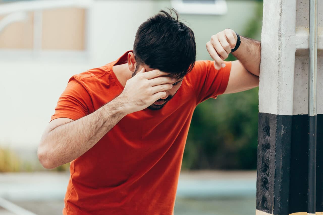 Man in red shirt leans on a pole while holding his head